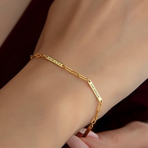 May include: Gold chain bracelet with two rectangular charms engraved with the words "DREAM" and "SOLAM".
