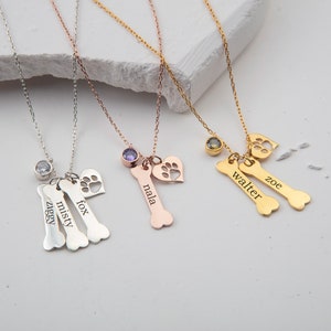 May include: Four silver, rose gold, and gold necklaces with personalized dog bone charms. Each charm has a different dog's name engraved on it: "Ziggy", "Misty", "Fox", "Nala", "Walter", and "Zoe".