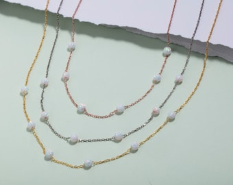 May include: Three delicate necklaces with a chain link design and small white opal beads. The necklaces are in gold, silver, and rose gold.