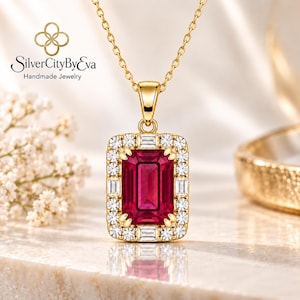 May include: A gold necklace featuring a rectangular pendant with a large emerald-cut red gemstone at the center, surrounded by a halo of small round and baguette-cut clear stones. The pendant hangs from a delicate gold chain, with SilverCityByEva text.