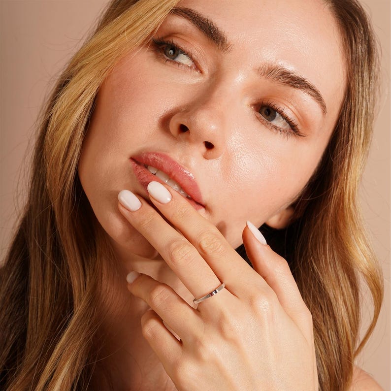 Pode incluir: Um close-up de uma m&atilde;o de mulher usando uma fina alian&ccedil;a de prata. O anel &eacute; simples e elegante, com um acabamento liso e polido.