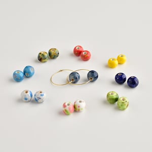 May include: A set of colorful ceramic beads with a pair of gold hoop earrings. The beads are in various colors, including blue, green, yellow, red, and white. The beads have a speckled or marbled pattern.