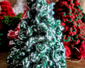 May include: A green and white crocheted Christmas tree ornament. The tree is made of yarn and has a fluffy texture.