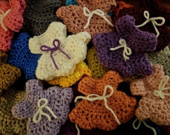May include: A close-up of a pile of colourful, handmade crochet baby booties. The booties are in shades of pink, purple, orange, and cream, each with a small white bow. The image highlights the texture and detail of the yarn used in the crafting process.