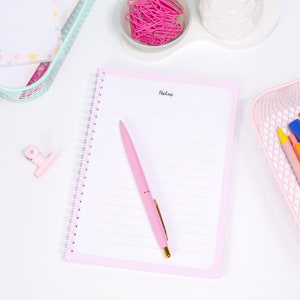 Może przedstawiać: R&oacute;żowy notes w spirali z napisem "Notes" na g&oacute;rze strony. R&oacute;żowy długopis ze złotą końc&oacute;wką leży na notesie.