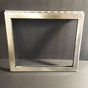 Puede incluir: Un marco de metal plateado con una parte superior con bisagras. El marco es rectangular y tiene un acabado liso y cepillado.