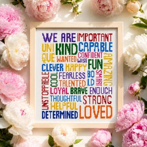 May include: A framed cross-stitch sampler featuring a grid of colorful words including WE ARE IMPORTANT, KIND, CAPABLE, UNIQUE, WANTED, CONFIDENT, WISE, FUN, CLEVER, HAPPY, FEARLESS, BOLD, AMAZING, COOL, TALENTED, LOYAL, BRAVE, ENOUGH, THOUGHTFUL, STRONG, HELPFUL, DETERMINED, LOVED.