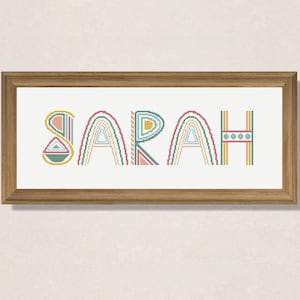 Op de afbeelding: Een ingelijst kruissteekontwerp met de naam "SARAH" in kleurrijke, geometrische letters. De letters zijn gestyled met regenboogachtige patronen en geometrische vormen.
