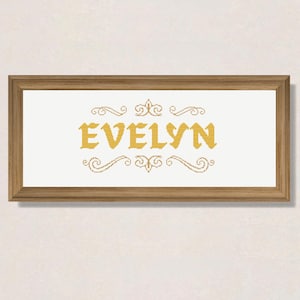 Puede incluir: Un diseño de punto de cruz enmarcado con el nombre "EVELYN" en una fuente dorada con adornos decorativos arriba y abajo del nombre.
