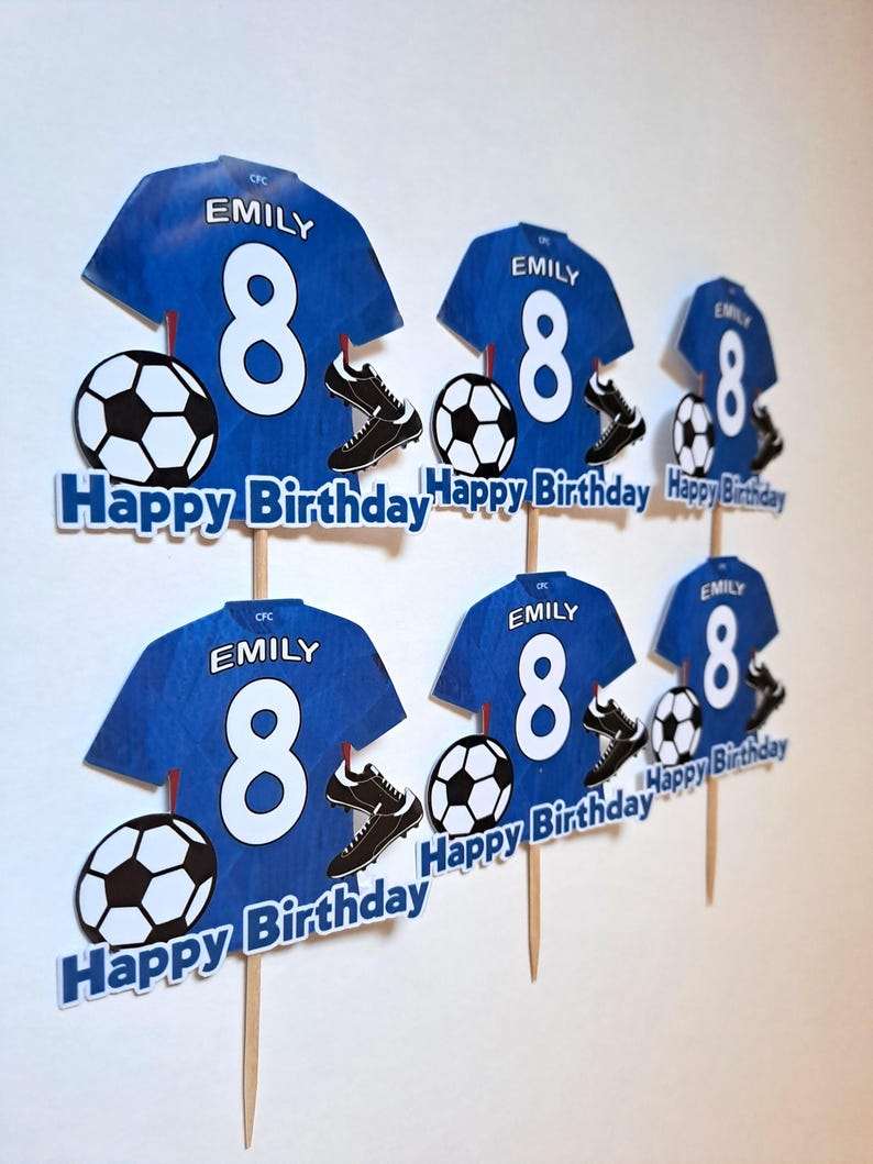 May include: Blue soccer-themed birthday cake toppers featuring a jersey with the name "EMILY" and the number "8", soccer balls, and cleats. The toppers also include the text "Happy Birthday".
