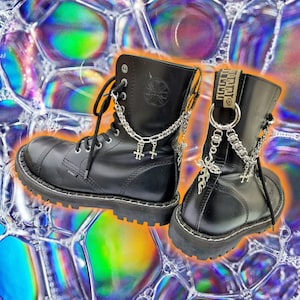 May include: A pair of black leather boots with silver chain and cross charms. The boots have a thick rubber sole and a lace-up closure.
