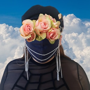 May include: A navy blue face mask with silver chains attached to the sides. The mask is decorated with pink and white roses.