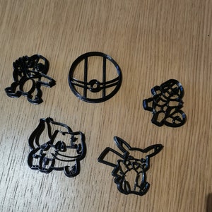 Puede incluir: Cinco cortadores de galletas impresos en 3D de color negro con forma de personajes de Pokémon. Los cortadores incluyen una Poké Ball, Bulbasaur, Charmander, Squirtle y Pikachu.