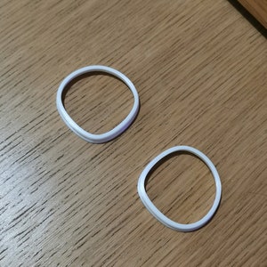 Puede incluir: Dos anillos de plástico blanco, posiblemente para un proyecto de manualidades o un juguete.