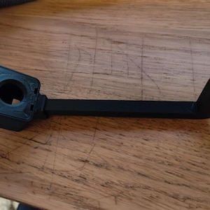 Puede incluir: Un soporte de cámara de plástico negro con una abertura circular y un brazo largo que se extiende hacia la derecha.