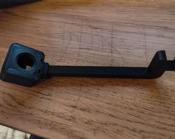 Puede incluir: Un soporte de cámara de plástico negro con una abertura circular y un brazo largo que se extiende hacia la derecha.