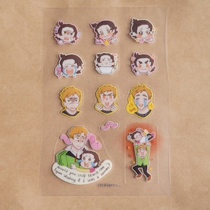 May include: A set of 10 colorful stickers featuring cartoon characters with different expressions. The stickers are printed on clear plastic and have a glossy finish. The stickers feature a character with blonde hair and blue eyes. The text on the sticker reads "would you still teach me figure skating if I won a grammy?"