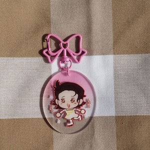 May include: Pink and white cartoon character keychain with a pink bow. The character has brown hair, brown eyes, and is wearing a yellow dress.