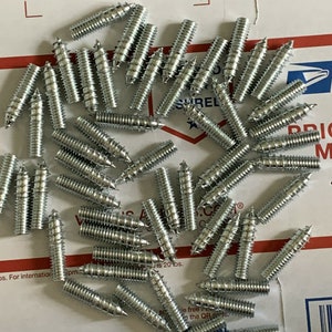 May include: A pile of silver-colored metal screws with a pointed tip and a threaded shaft. The screws are arranged in a random pattern on a white surface.