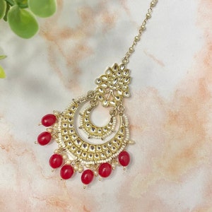 May include: Gold and red Indian bridal headpiece with a chain and a large, ornate pendant with red beads.