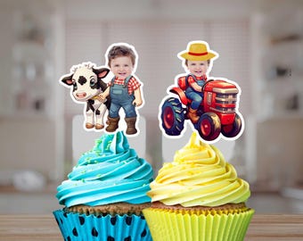 May include: Two cupcakes decorated with edible images. One cupcake has blue frosting and a cow and farmer image. The other cupcake has yellow frosting and a tractor and farmer image.
