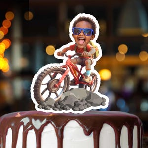 May include: A cake topper featuring a cartoon illustration of a child riding a red bicycle. The child wears blue sunglasses and is smiling. The cake is white with chocolate frosting.