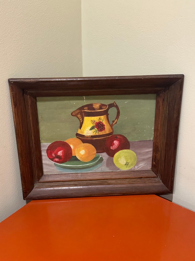 May include: A framed painting of a still life with a brown pitcher, red and yellow apples, and a green plate on a green background. The painting is signed "L. Griffin".