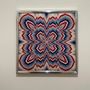 Könnte beinhalten: Ein gerahmtes Nadelbild mit einem geometrischen Muster in Blautönen, Rot und Weiß. Das Design ist symmetrisch und erzeugt ein Gefühl von Tiefe und Bewegung.