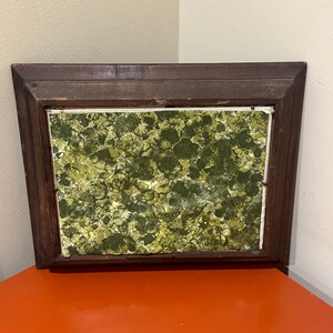 May include: A framed square picture with a green and yellow abstract design. The frame is dark brown wood.