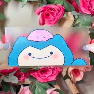 May include: A transparent sticker with a cartoon Snorlax and Ditto design. Snorlax is blue with a cream face and pink cheeks. A pink Ditto sits on top. The sticker has the text "@ploofferfish".
