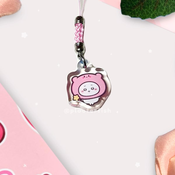 May include: A clear acrylic charm featuring a cute cartoon character in a pink bear costume. The charm has a pink braided lanyard and a silver-tone metal clasp. The character has a star and the text "@plootofish".