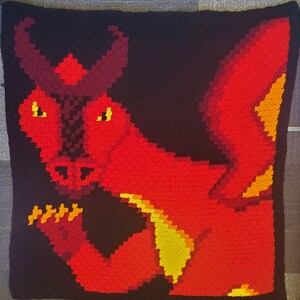 May include: A red and yellow crocheted dragon with horns and a black background.