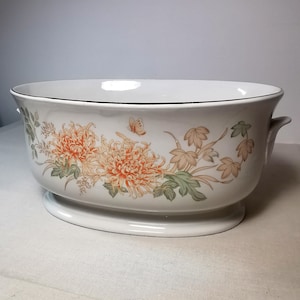 May include: White ceramic serving bowl with a floral design featuring orange chrysanthemums, green leaves, and a butterfly. The bowl has a black rim and two small handles. The oval base is 30 cm long.
