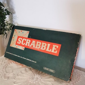 Pode incluir: Uma caixa de jogo Scrabble vintage em verde escuro com um logotipo vermelho e branco. A caixa apresenta a palavra "SCRABBLE" em letras grandes e em negrito. A caixa do jogo é fabricada por J.W. Spear & Sons, Ltd. em Enfield, Middlesex, Inglaterra.