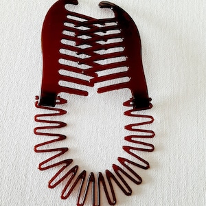 May include: A brown plastic hair comb with a curved design and a series of teeth on one side. The comb has a circular shape and is designed to hold hair in place.
