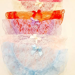 May include: A stack of six pairs of lace underwear in various colors: pink, cream, orange, purple, light pink, and blue. Each pair features a decorative bow with a pearl accent. The delicate lace and soft colors create a feminine aesthetic.