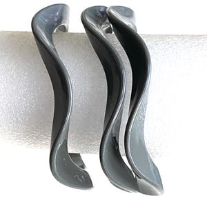 May include: Three gray plastic bangle bracelets with a wavy design.