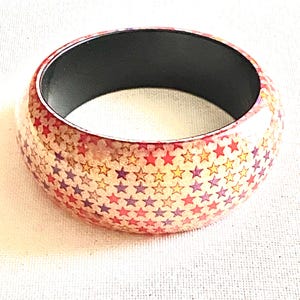 May include: A red wooden bangle with a black interior and a pattern of multi-colored stars.