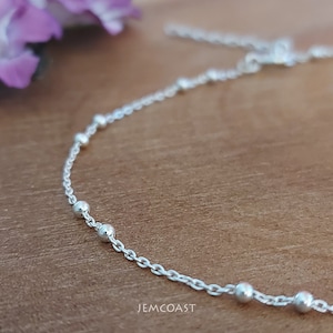 May include: A silver chain bracelet with small round beads. The bracelet is on a wooden surface.