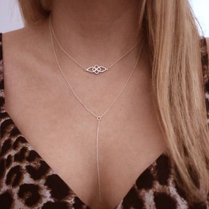 Può includere: Due collane d'argento con una catena delicata e un piccolo ciondolo con un designo a nodo intricato. La collana più lunga ha un semplice ciondolo circolare all'estremità.