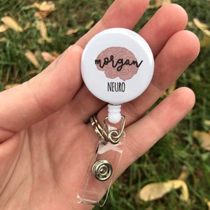 May include: White retractable badge holder with a round button featuring a pink brain graphic and the text "morgan" and "NEURO".
