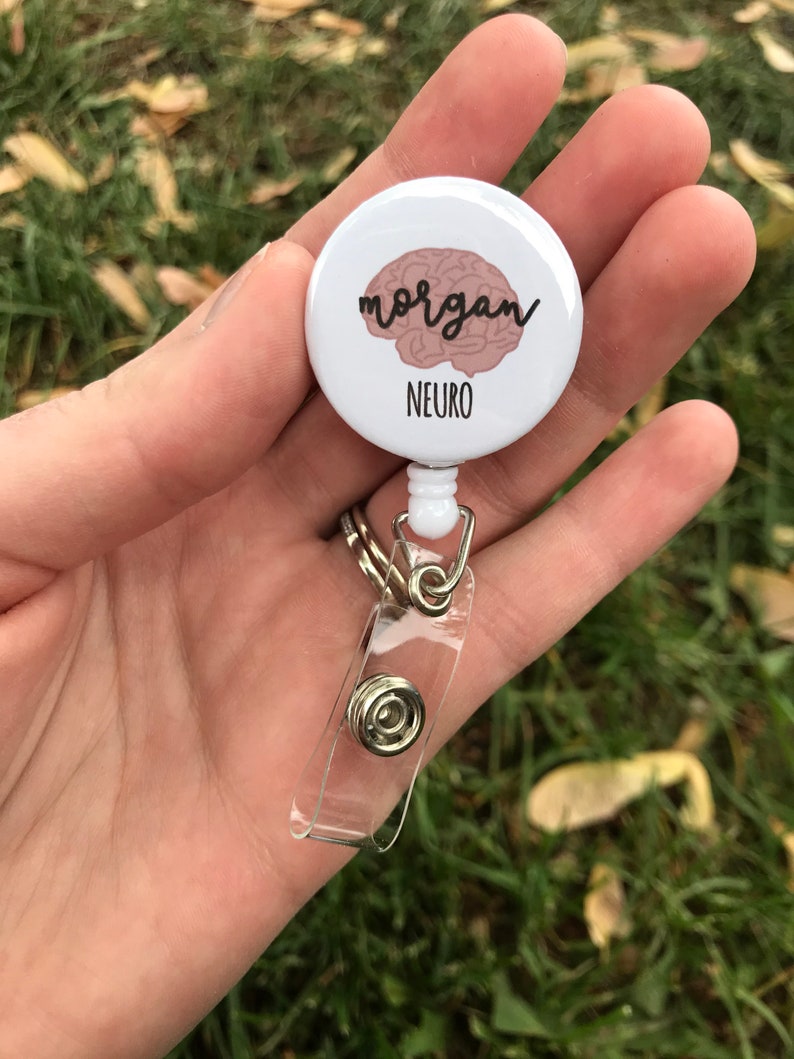 May include: White retractable badge holder with a round button featuring a pink brain graphic and the text "morgan" and "NEURO".