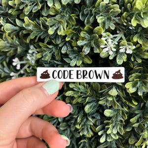 May include: A white sticker with a brown poop emoji on each side and the text "CODE BROWN" in black.