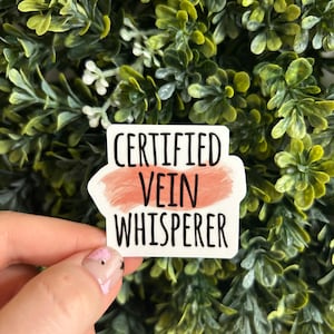Puede incluir: Pegatina blanca con el texto "CERTIFIED VEIN WHISPERER" en letras negras. El texto está sobre un fondo de acuarela rosa.