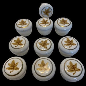 May include: Ten white ceramic cabinet knobs with gold trim and a gold leaf design.