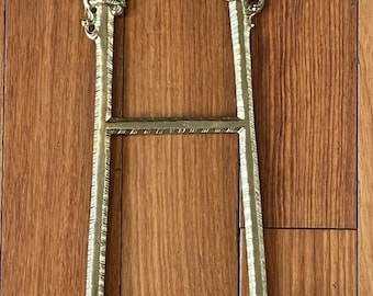 Peut inclure: Chevalet doré orné de volutes et de motifs floraux complexes. Le chevalet présente une base et un sommet décoratifs, avec deux supports verticaux et une barre horizontale. Le design est vintage et élégant, adapté à l'exposition d'œuvres d'art ou d'objets décoratifs.