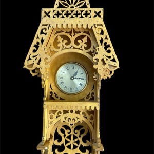 May include: A wooden wall clock with an ornate, openwork design. The clock face is round with Roman numerals. The clock has a decorative top and a shelf at the bottom. The wood has a light brown color.