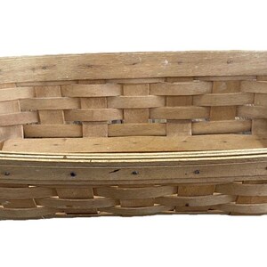May include: A rectangular, light brown woven basket with a slightly rounded rim. The basket is made of interwoven wooden strips, creating a textured surface. The basket is empty and sits on a white background.