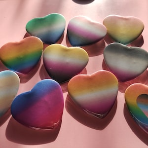 May include: A selection of heart-shaped items with a gradient of colours, including blue, green, yellow, orange, and pink. The hearts are arranged on a pink surface, creating a vibrant and colourful display.