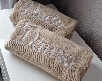 Könnte beinhalten: Zwei beige Handtücher mit den Namen "Vlad" und "Denisa", die in Weiß gestickt sind.
